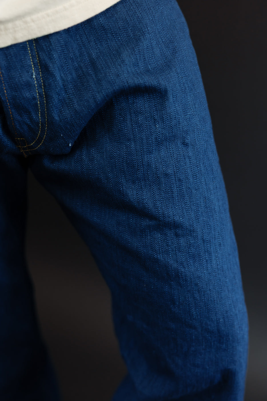 Close-up side view of men's selvedge denim jeans, showcasing texture and gold stitching on thigh