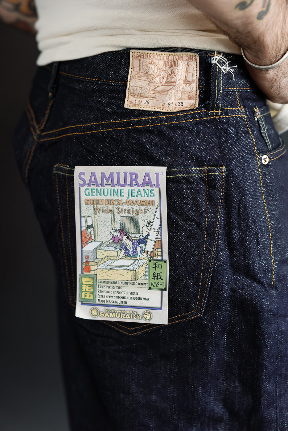 Close-up of male model's back showing Samurai Genuine Jeans label, indigo denim, and stitching details.