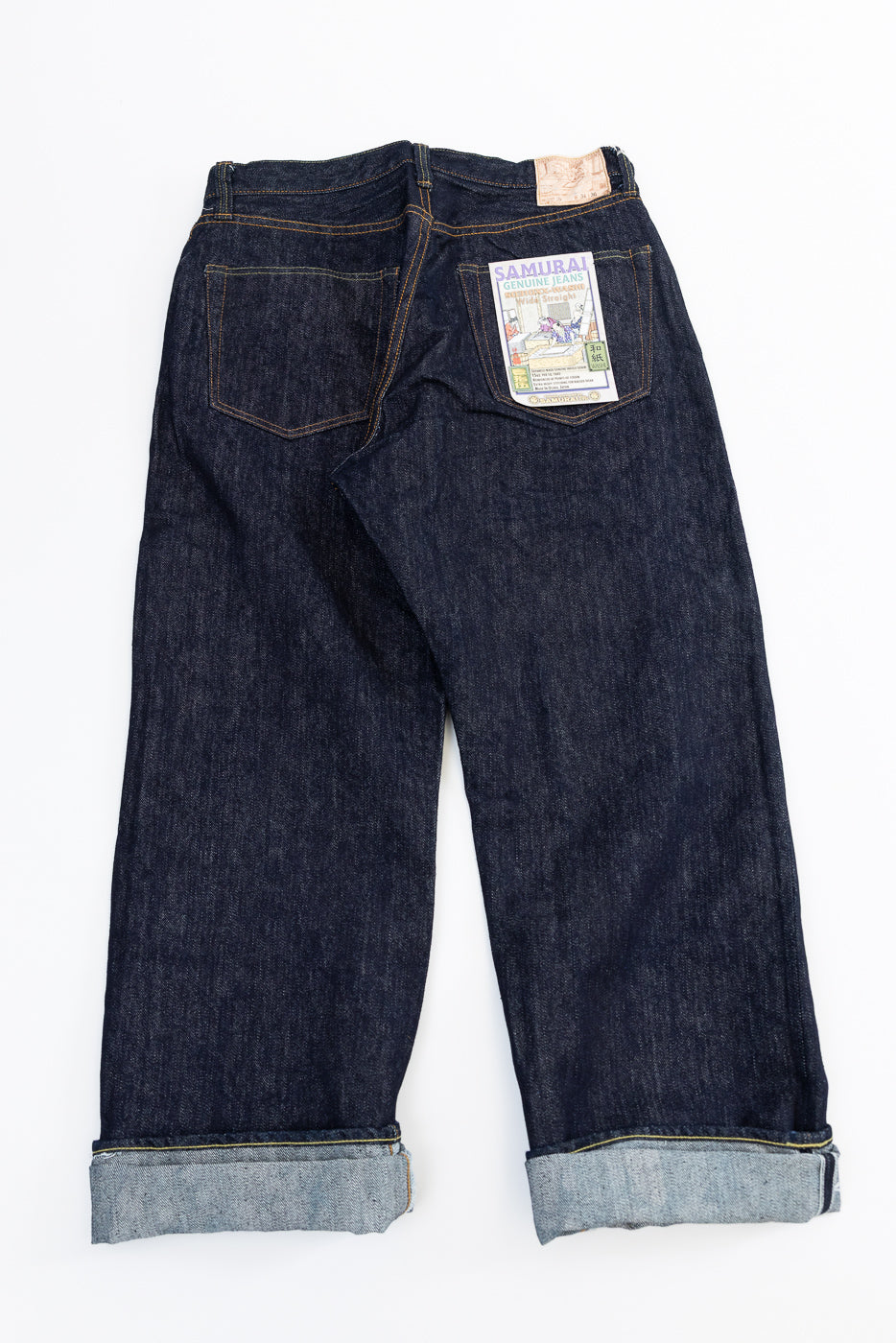 Back view flat lay of dark selvedge denim jeans, cuffed hems, Samurai patch on right pocket
