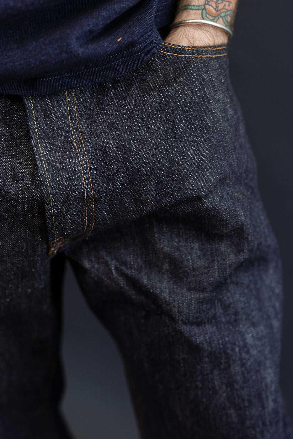 Close-up front view of dark selvedge denim jeans on male model, showing orange stitching and fabric texture