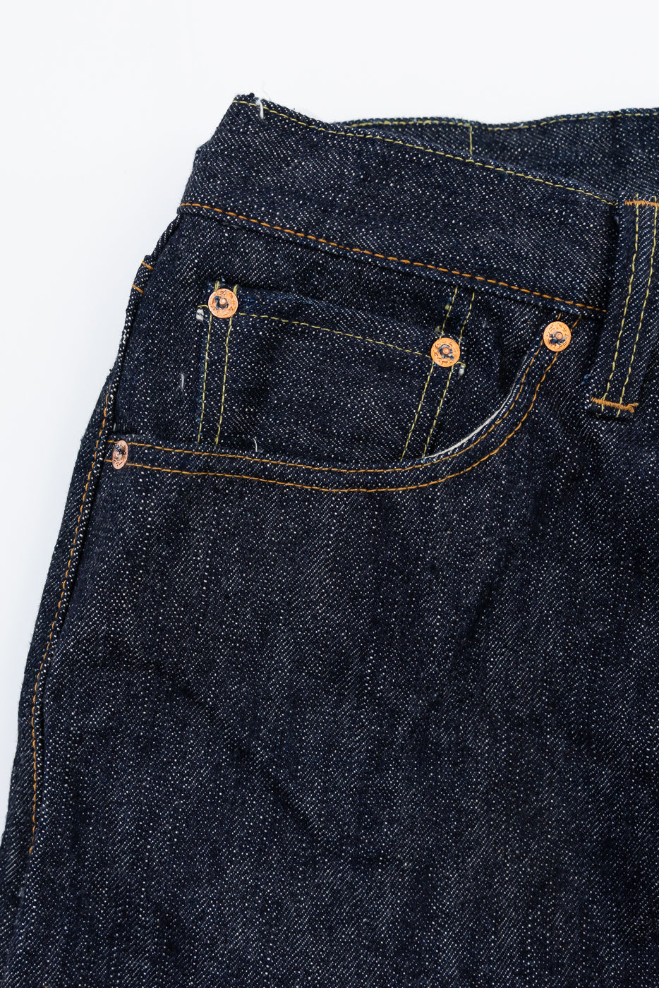 Close-up front view of dark selvedge denim jeans showing copper rivets, yellow stitching, and fabric texture