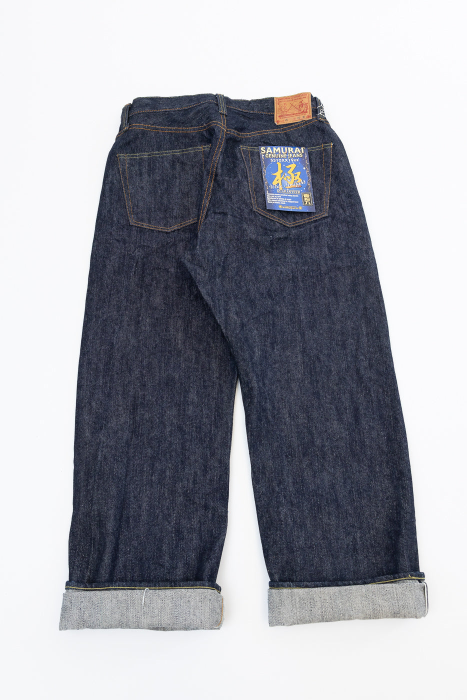 Back view flat lay of dark selvedge denim jeans, cuffed hem, Samurai brand patch on right pocket
