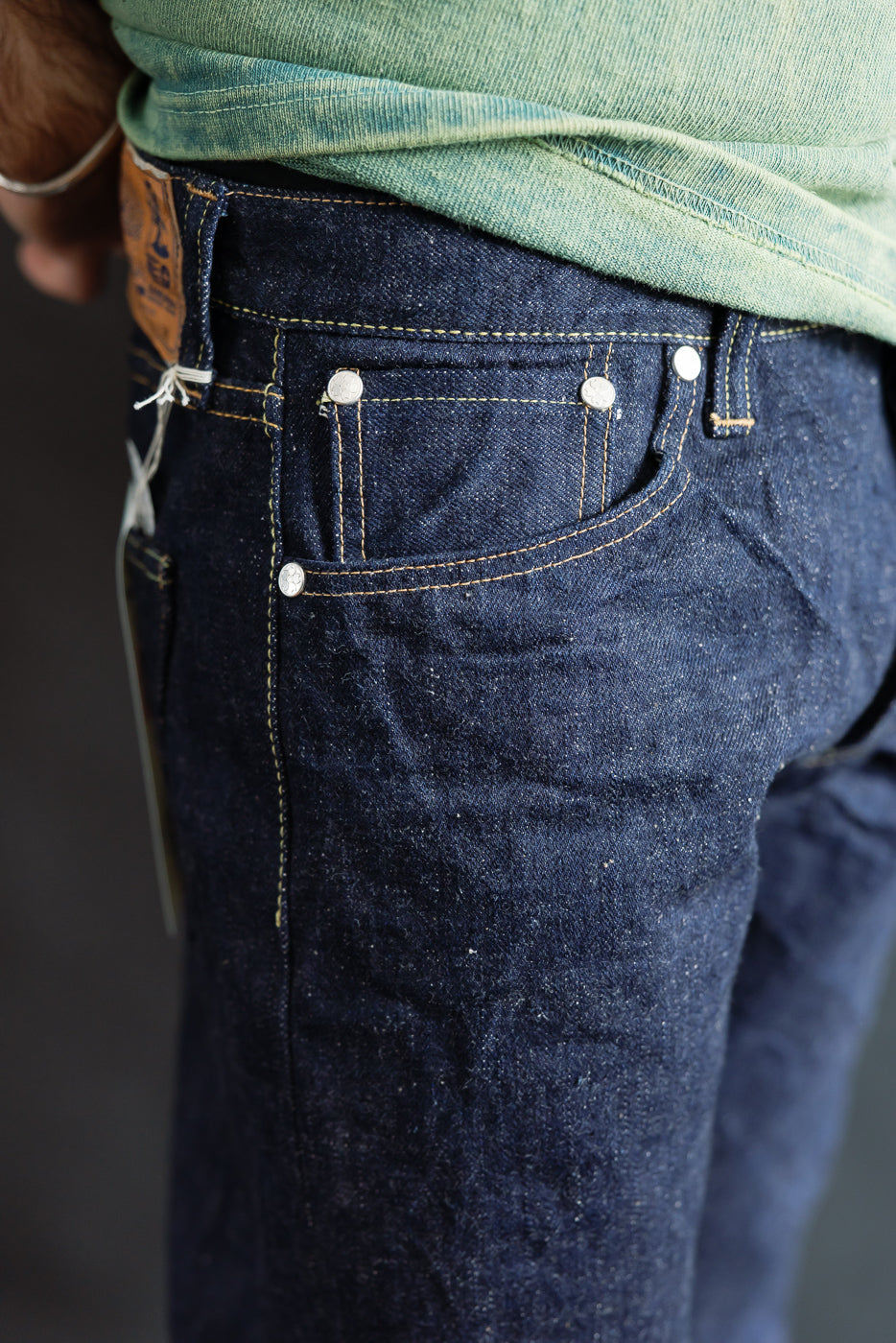 Close-up of male model’s right hip in raw selvedge denim jeans, showing coin pocket, rivets, and visible denim texture. Model is 5'9