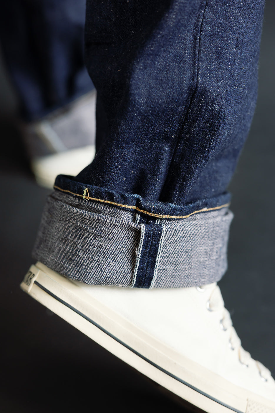 Close-up of male model’s cuffed selvedge jeans hem, front side view, showing denim texture and stitching detail, model is 5'9