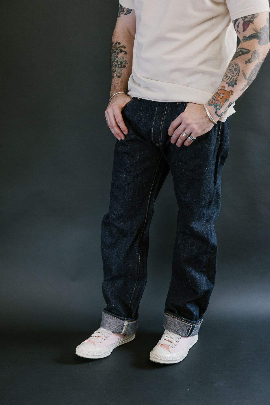 Person wearing Samurai S500AX-SAKURA 18oz Ai-Plus-Sakura Selvedge Jeans, showcasing deep indigo denim with sakura-dyed undertones, rolled cuffs, and pink sneakers.