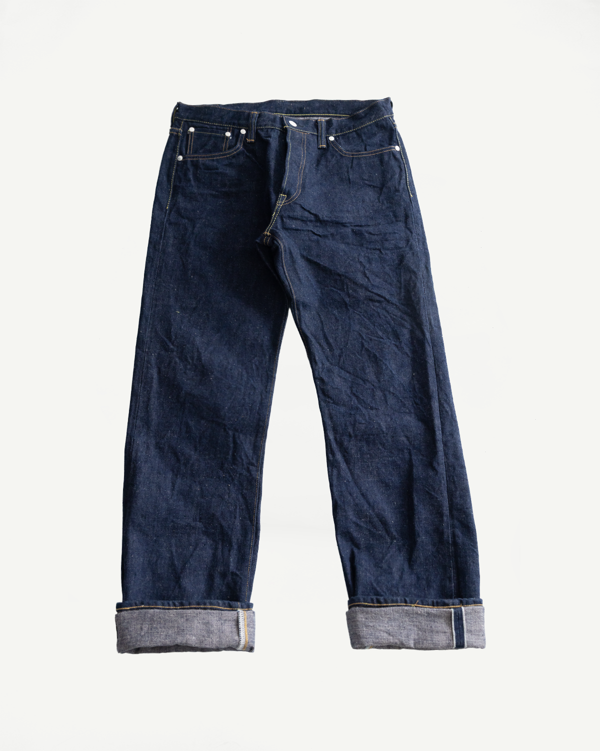 Flat lay front view of regular straight indigo selvedge jeans with cuffed hems and visible pocket rivets.