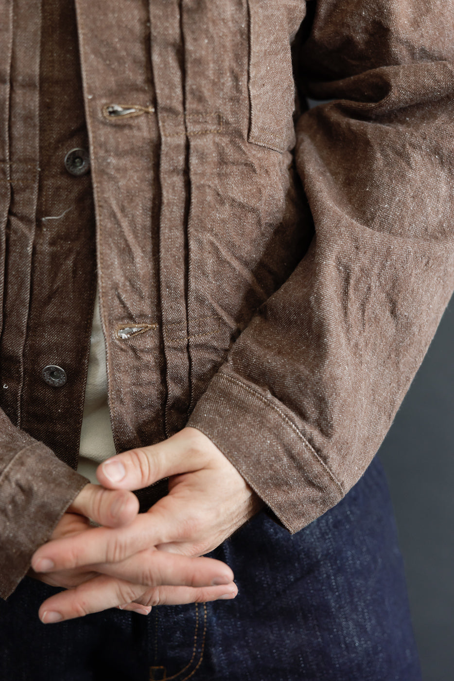 Close-up front view of brown work jacket on male model, showing button details, chest pocket, and textured fabric