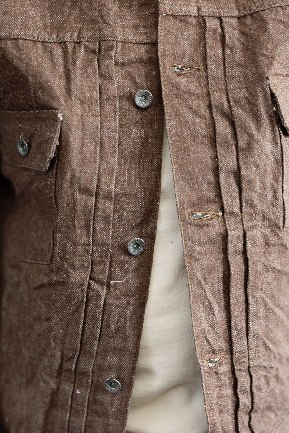 Close-up front view of brown work shirt with metal buttons, chest pocket, and selvedge fabric texture