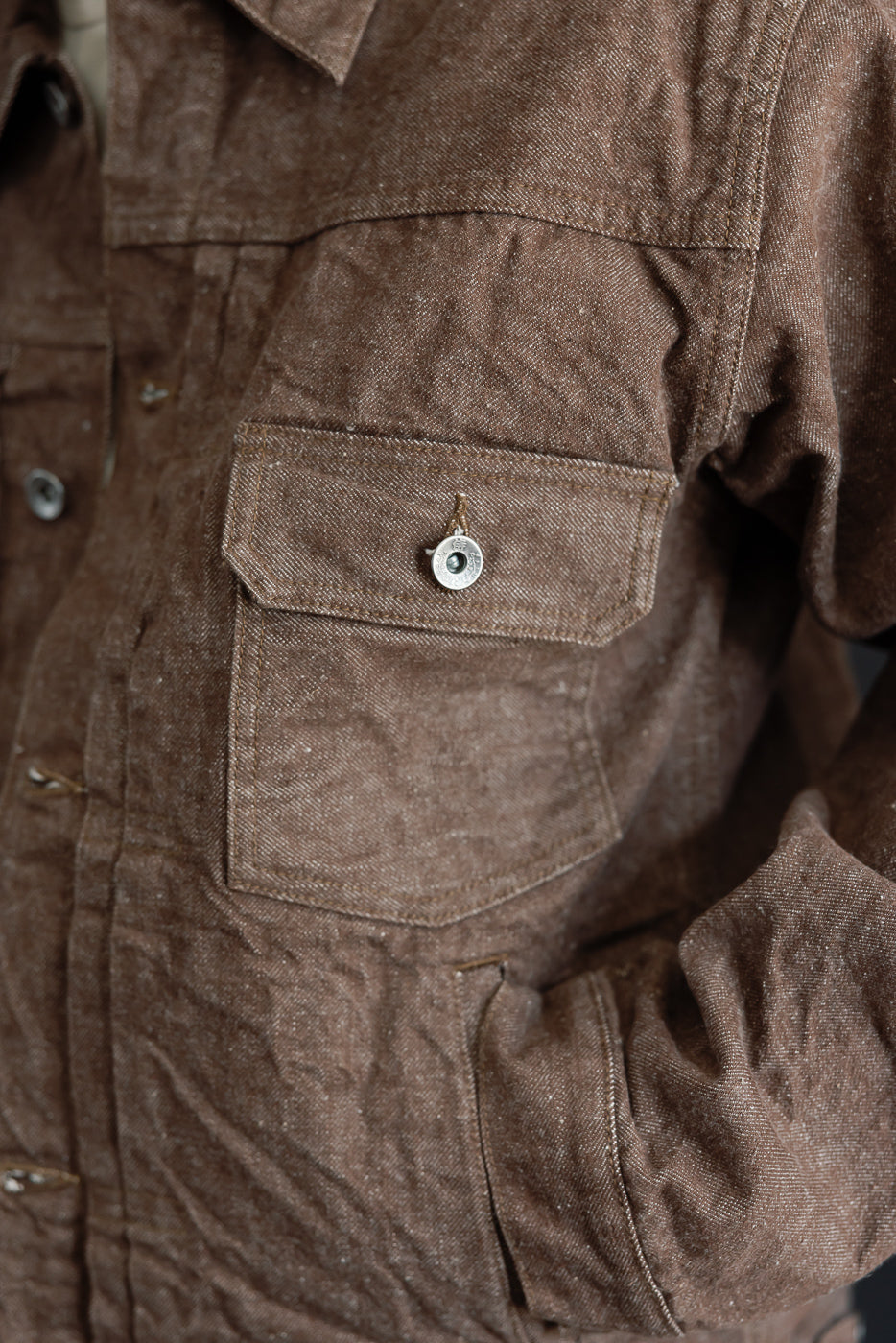 Close-up of brown shirt front, showing chest pocket with snap button, fabric texture, and stitching details.