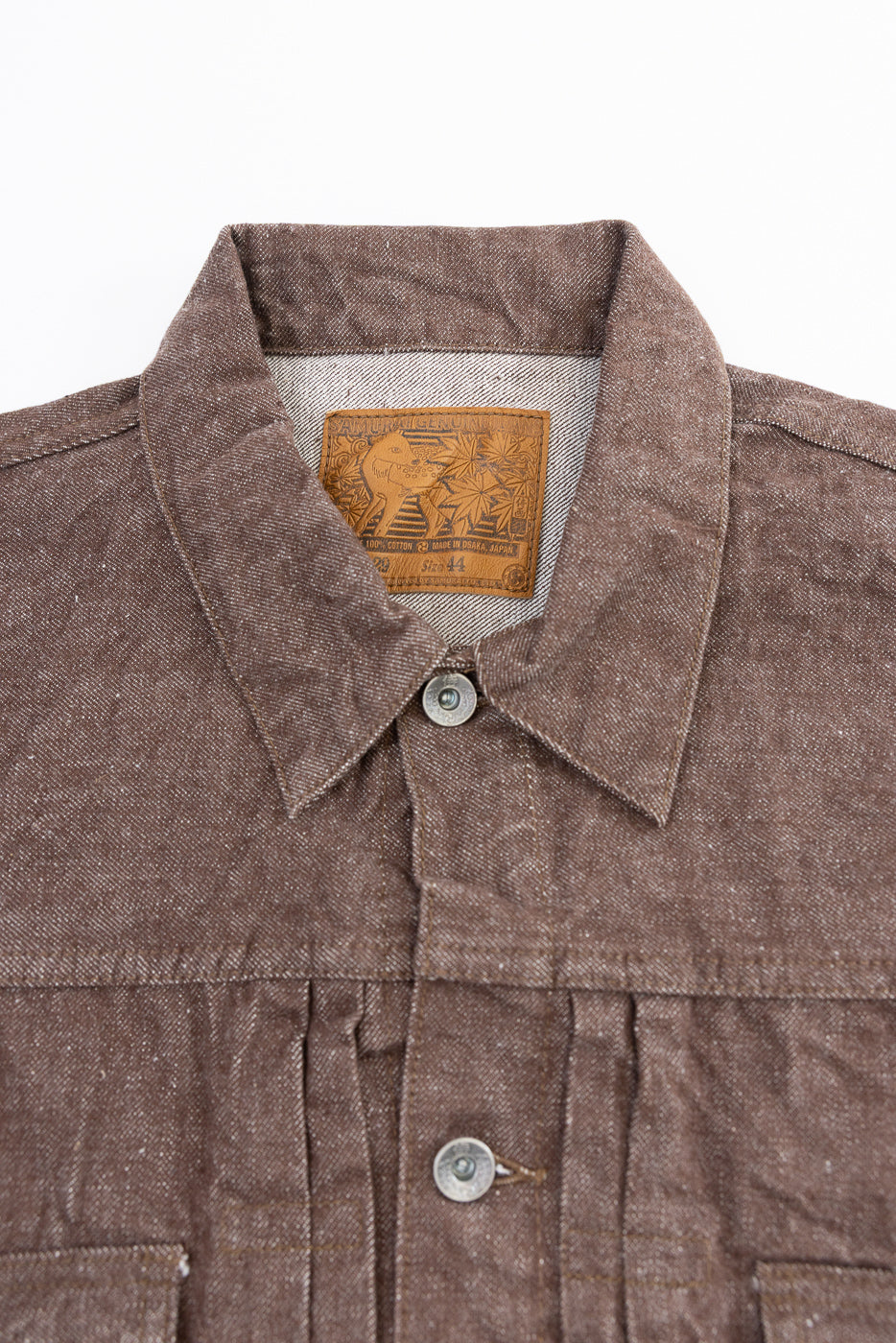 Close-up front view of brown selvedge work shirt collar, showing leather brand patch, button placket, and fabric texture