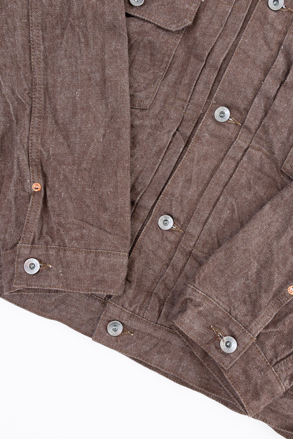 Close-up front view of brown selvedge denim jacket showing silver buttons, chest pockets, and fabric texture