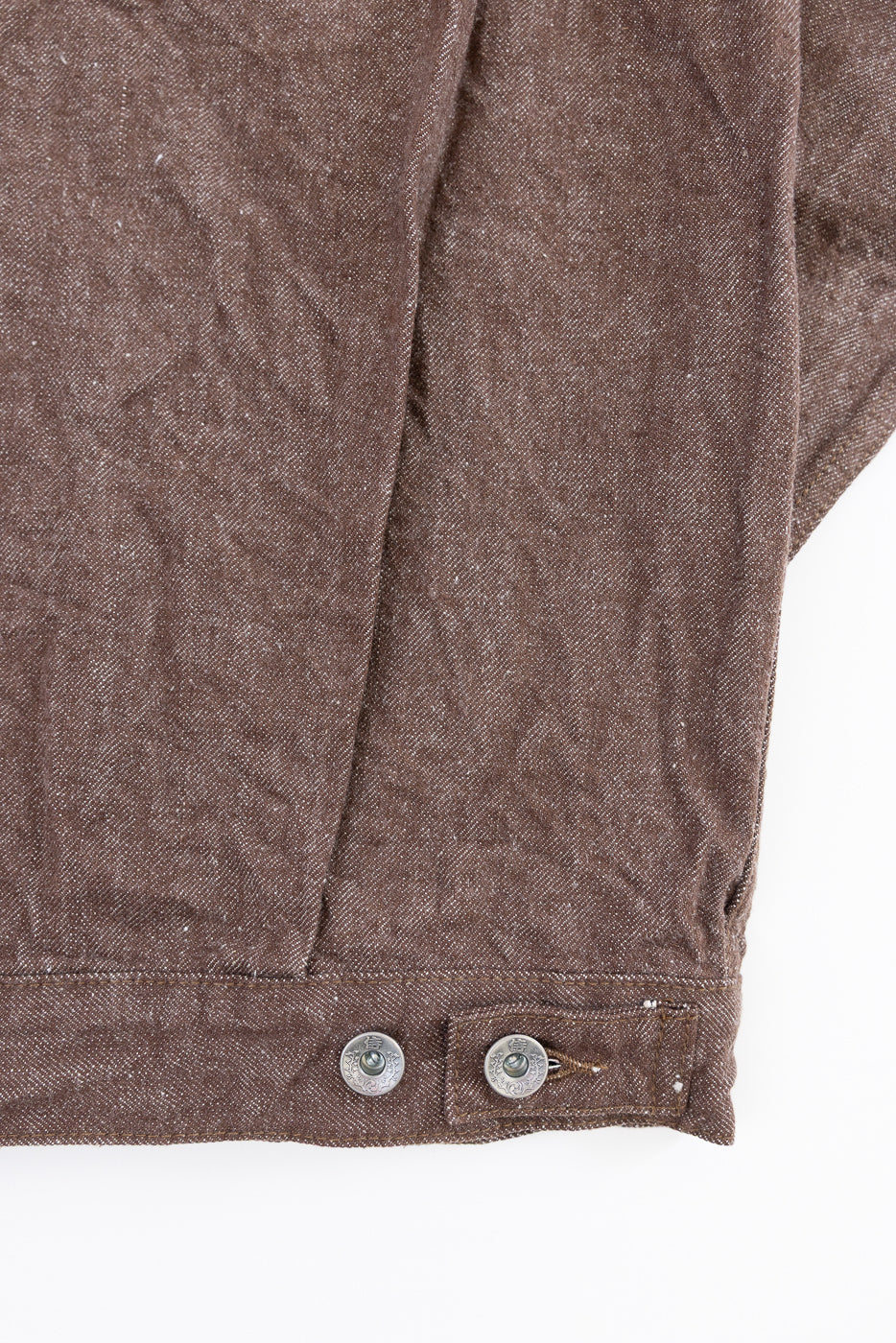Close-up front view of brown selvedge jacket hem with silver buttons and fabric texture