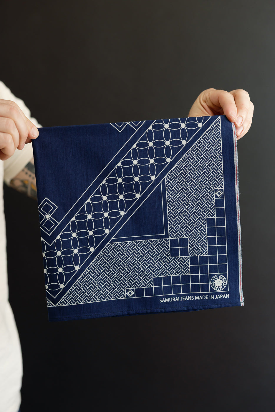 Close-up front view of navy blue Samurai Jeans bandana with white geometric patterns, held by male model, made in Japan
