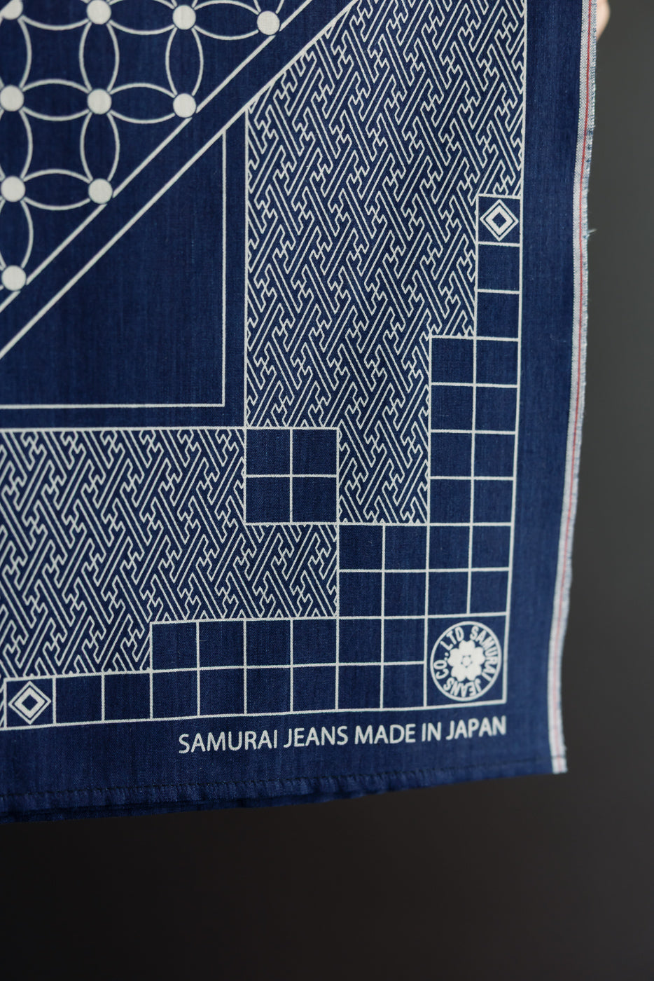 Close-up of Samurai Jeans indigo denim fabric with white geometric patterns, selvedge edge, and 'Made in Japan' tag detail.