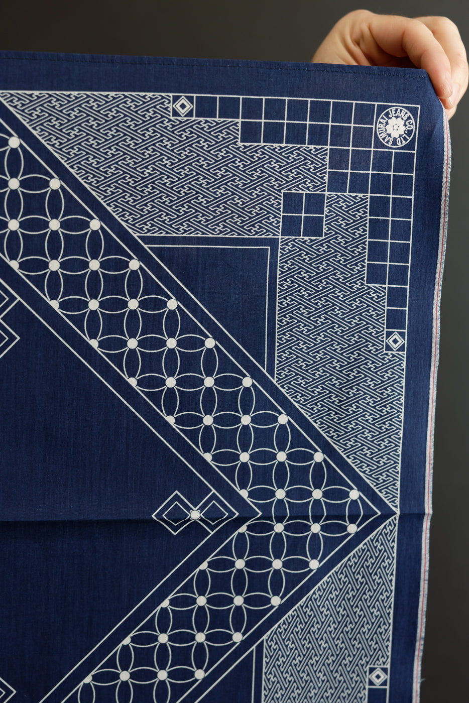 Close-up of indigo selvedge bandana front, showcasing geometric white patterns, tag detail, and fabric texture.