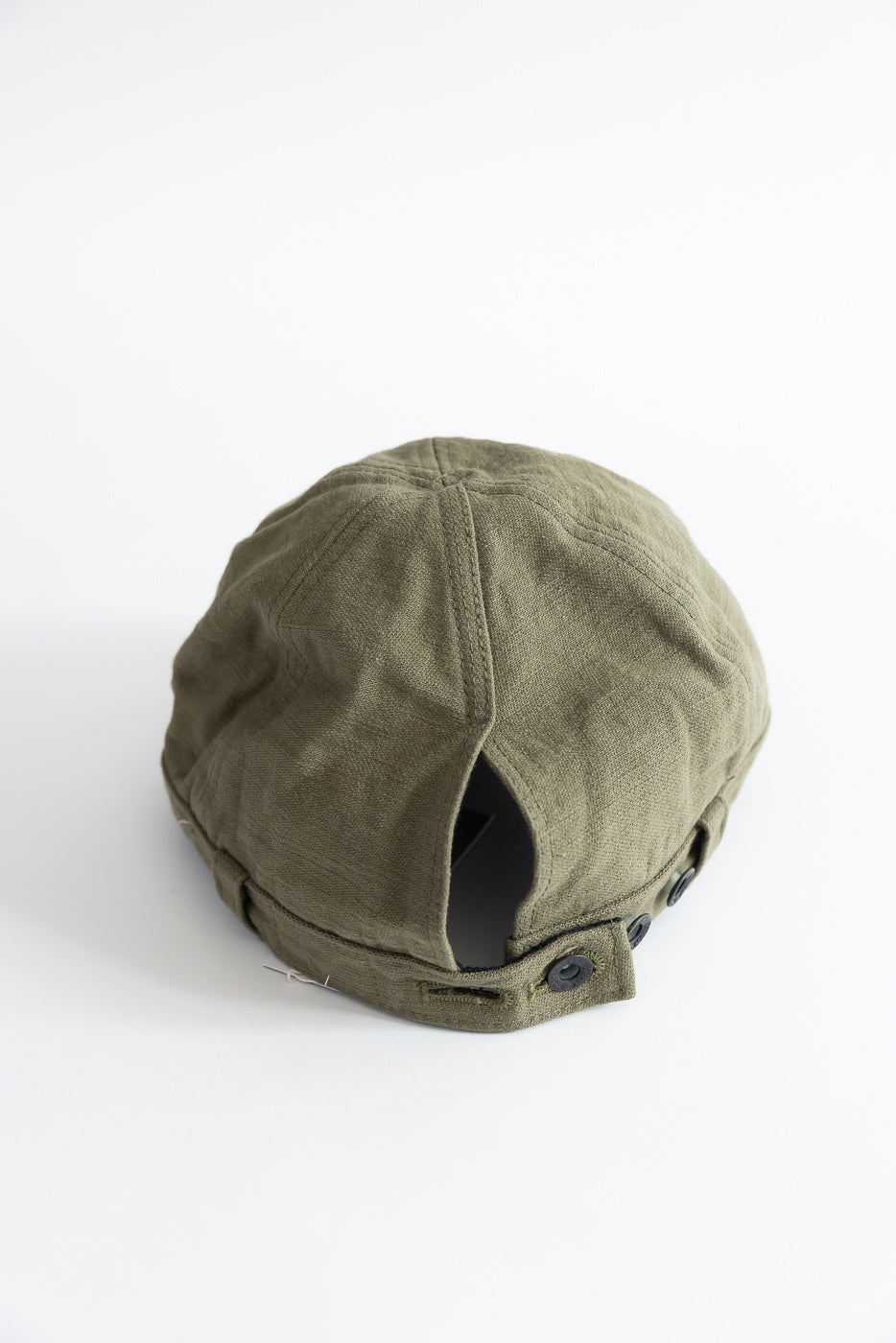 Close-up of back of olive workman’s cap, showing fabric texture and button adjustment