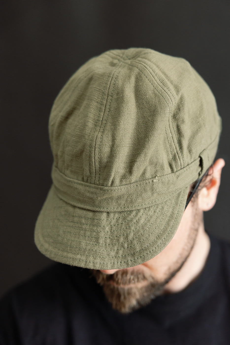 Close-up front view of olive heavy back satin work cap on male model, 5'9