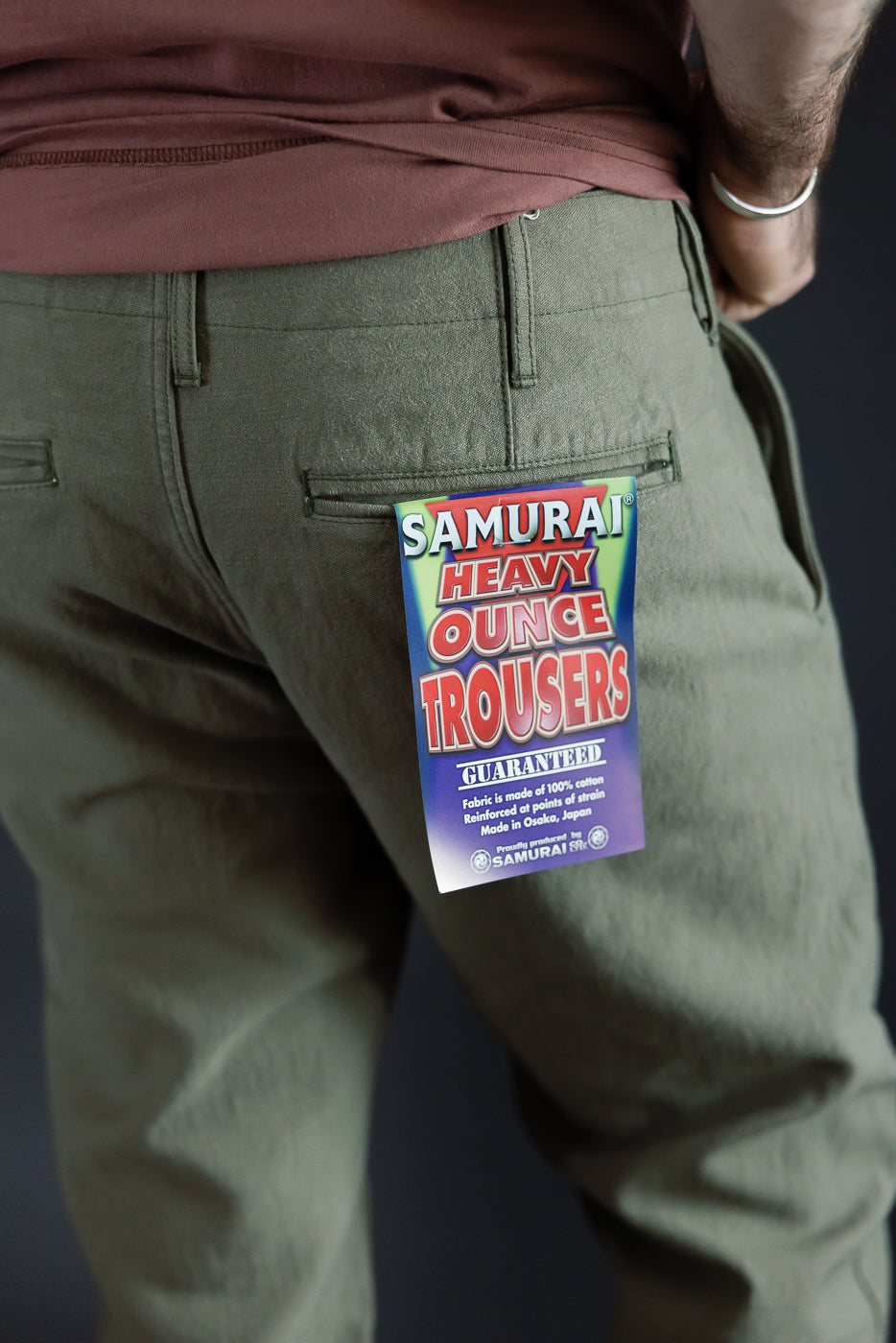 Back view of olive green Samurai Heavy Ounce Trousers on male model, tag visible, 100% cotton, made in Osaka.
