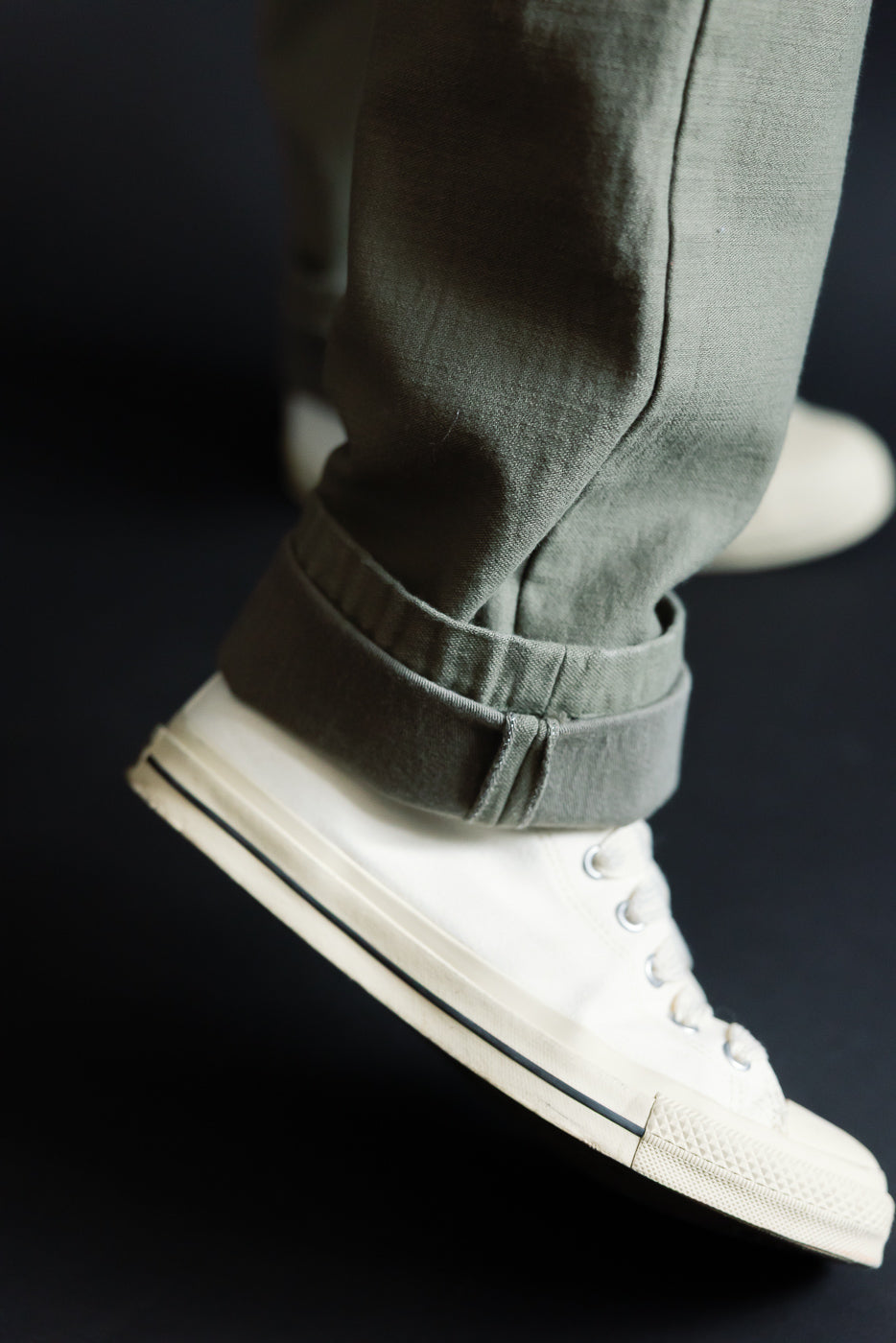 Close-up of olive pants cuff over white sneakers, male model, athletic build