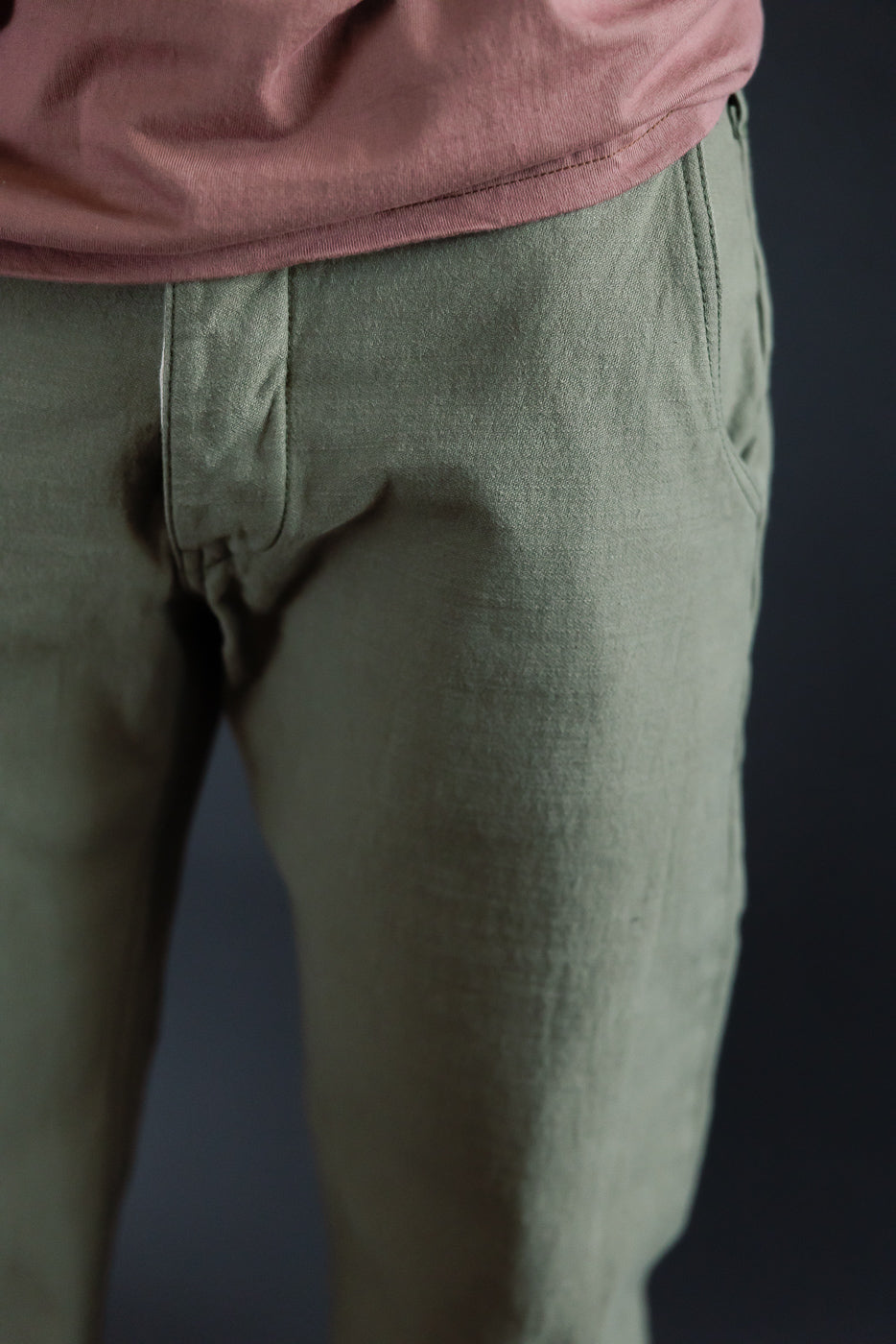 Close-up front view of male model's olive pants, showcasing fabric texture and fly detail.