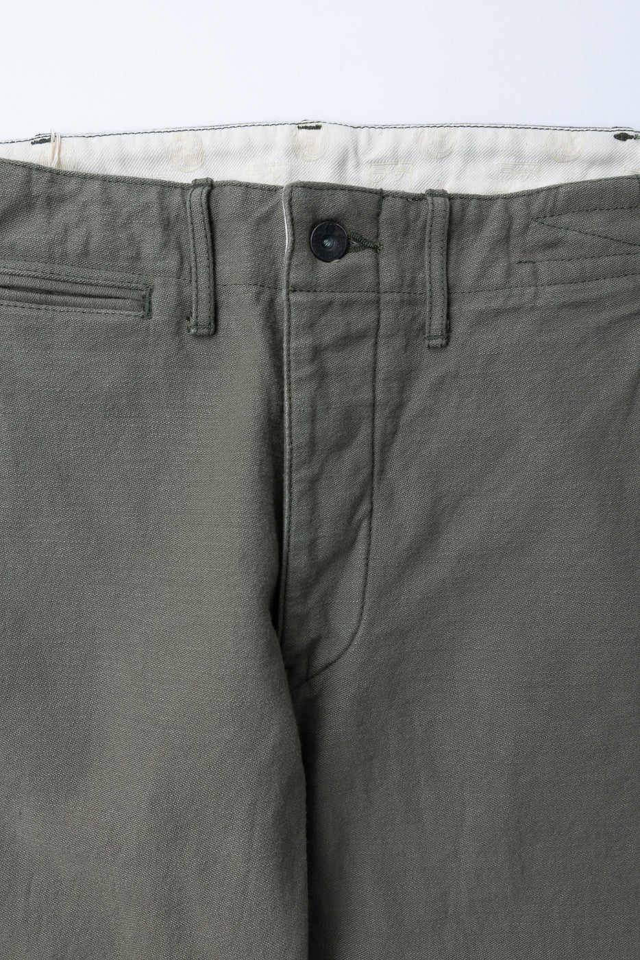 Close-up front view of olive green pants with button fly and textured fabric