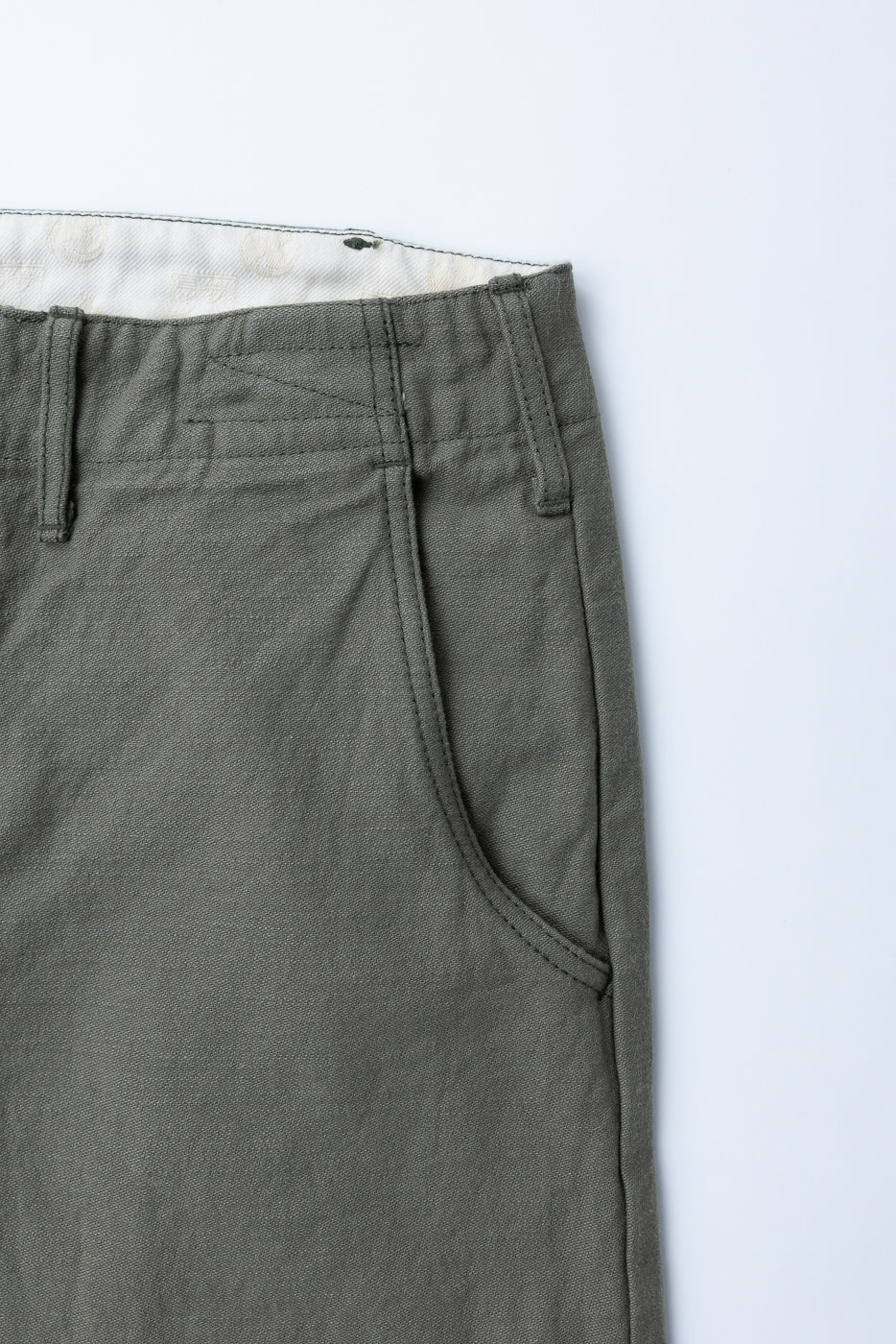 Close-up front view of olive green casual pants showing waistband, belt loops, and front pocket stitching detail