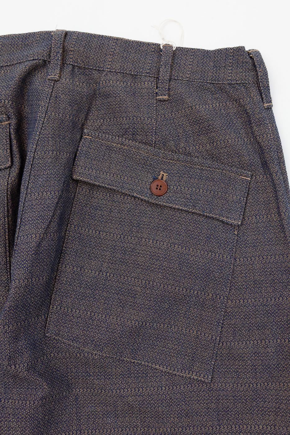 Close-up back view of men's selvedge trousers showing rear pocket with brown button and textured fabric weave