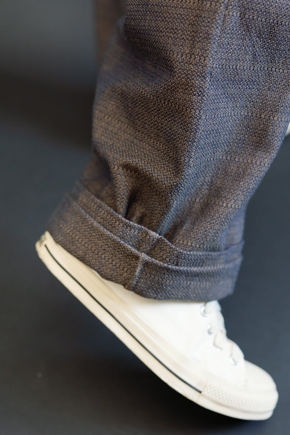 Close-up side view of male model's cuffed selvedge denim hem with white sneaker, showcasing fabric texture