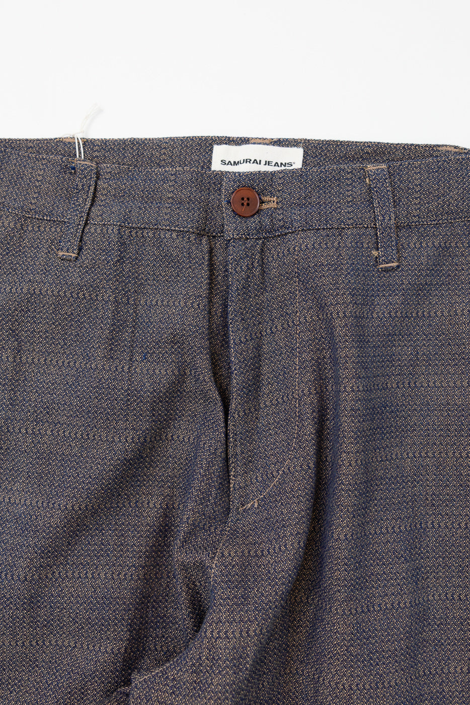 Close-up front view of Samurai Jeans selvedge trousers, showing button, tag, and textured denim weave