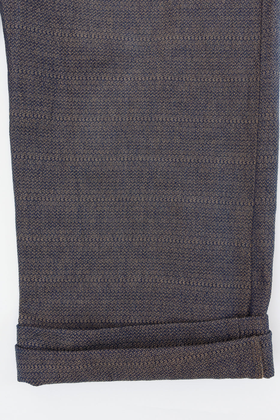 Close-up front view of dark selvedge pants hem with rolled cuff, showing textured weave and stitch detail
