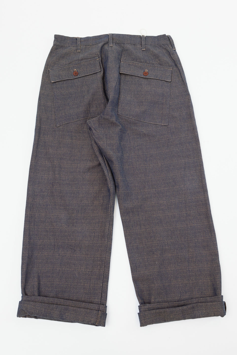 Back view flat lay of dark gray textured selvedge pants with buttoned rear pockets and cuffed hems