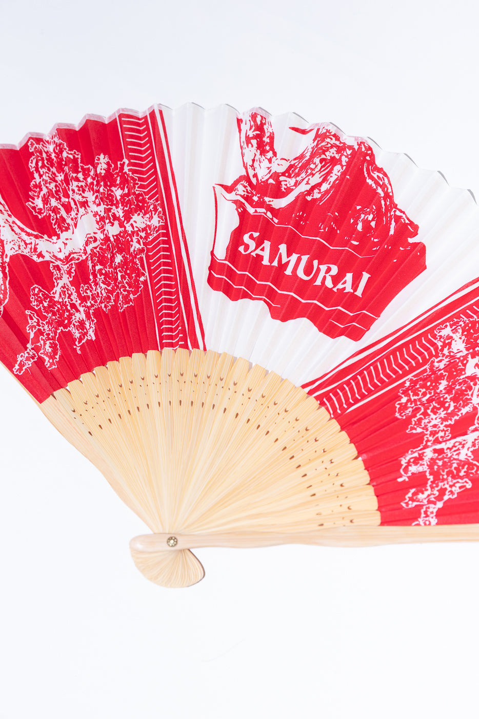 Close-up of a red and white folding hand fan with 'SAMURAI' text and Japanese art.