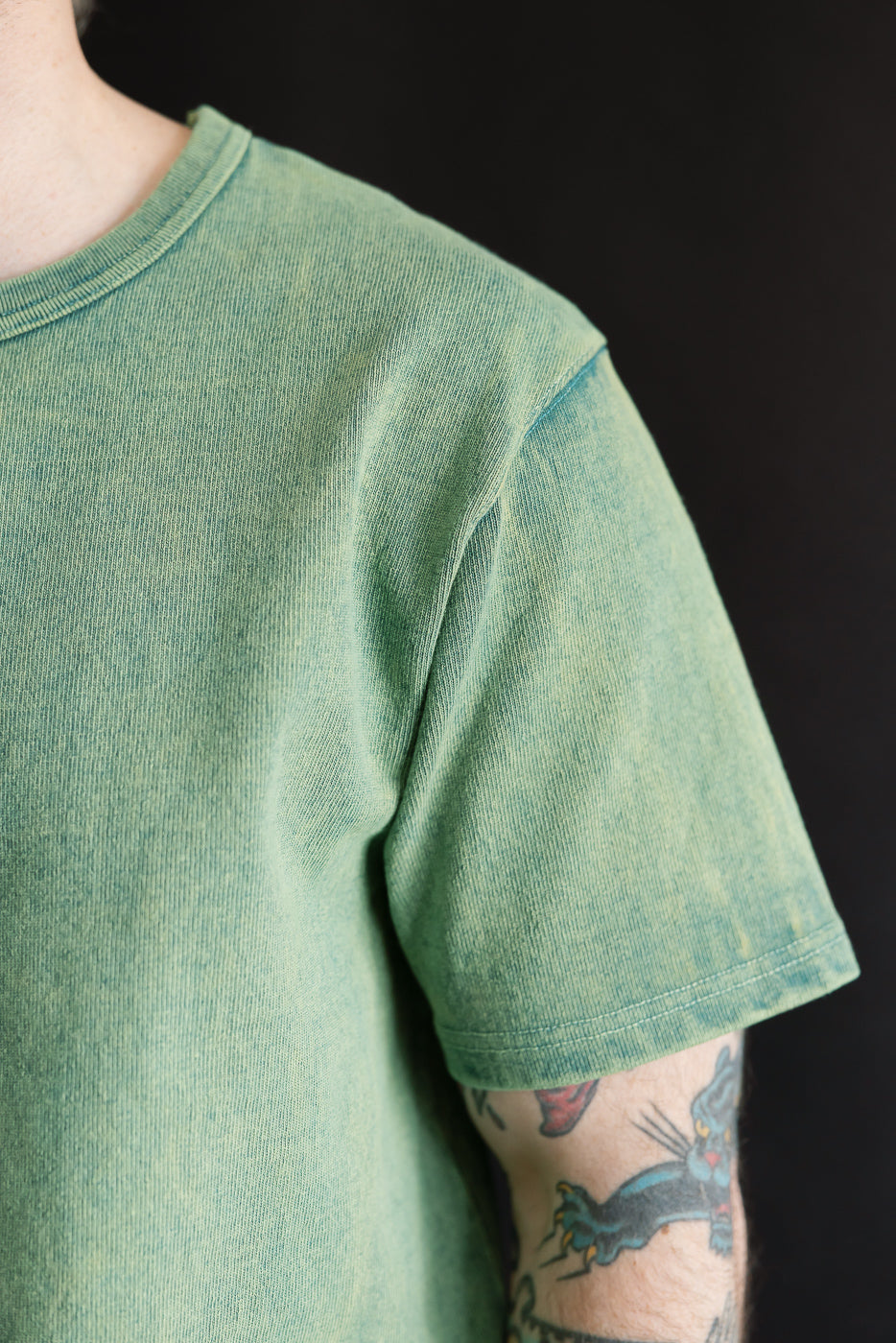 Close-up of the right shoulder and sleeve of a green heavy-weight t-shirt on a male model, 5'9