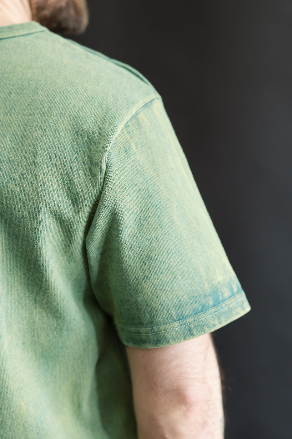 Close-up of male model’s right back shoulder wearing green heavy-weight T-shirt, sleeve and seam detail visible, model is 5'9