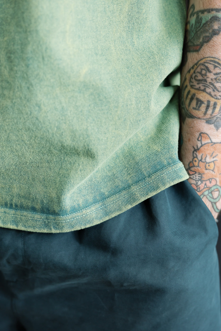 Close-up of hem detail, side view of green extra heavy t-shirt on male model, athletic build, 5'9