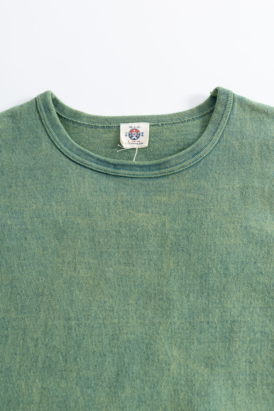 Close-up of front upper chest and collar on green extra heavy t-shirt, showing ribbed crewneck, fabric texture, and neck tag detail.