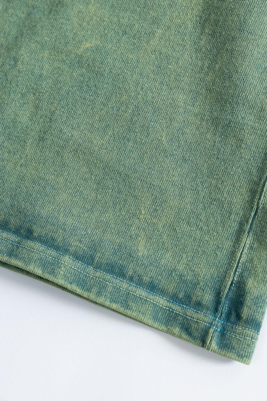 Close-up of green extra heavy t-shirt hem, showing fabric texture and stitching on front side.