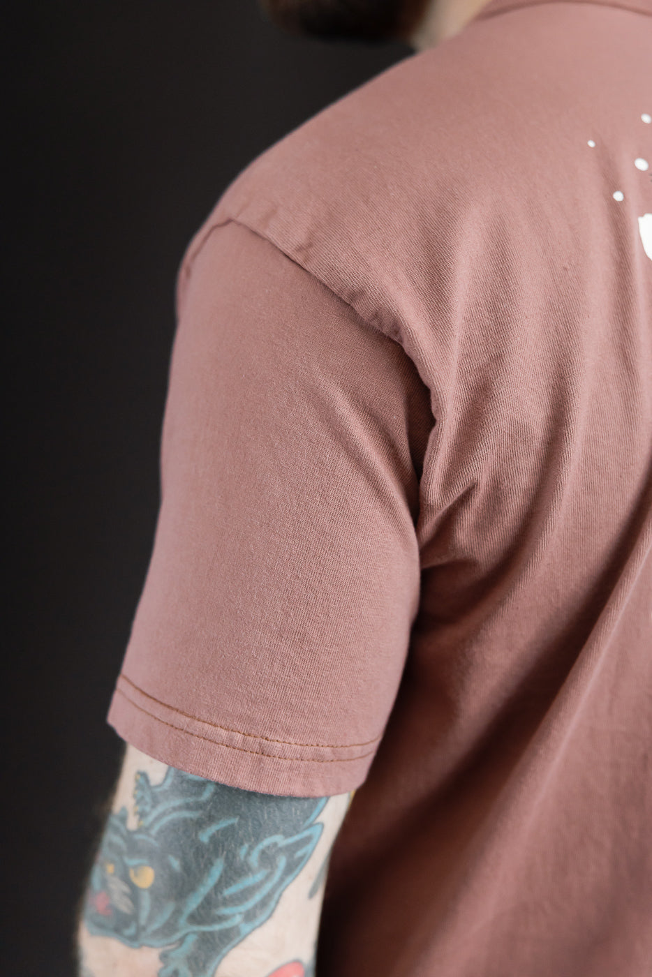 Close-up of male model's back, showcasing mauve t-shirt sleeve hem and shoulder seam detail.