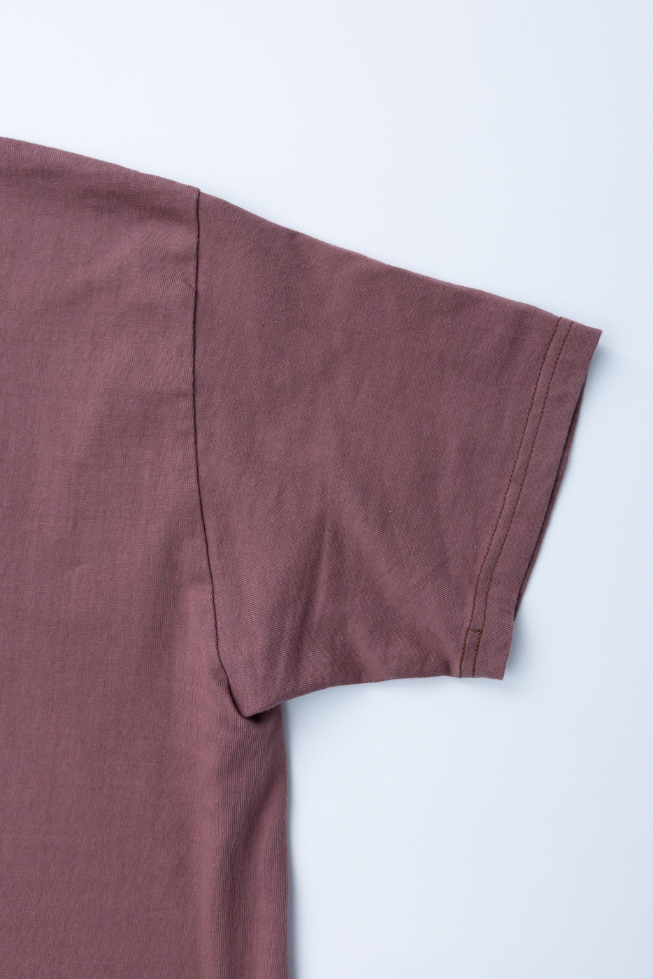 Close-up of dusty rose t-shirt sleeve hem, showing ribbed fabric texture and double-stitch detail on front.