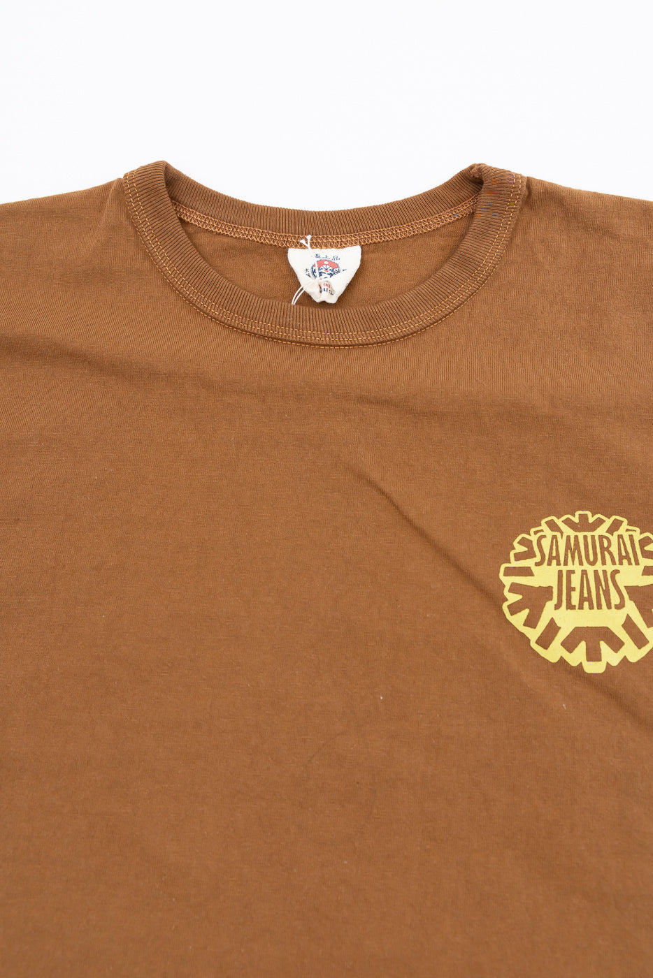 Close-up front view of brown tee with Samurai Jeans logo, ribbed crew neck, and tag detail