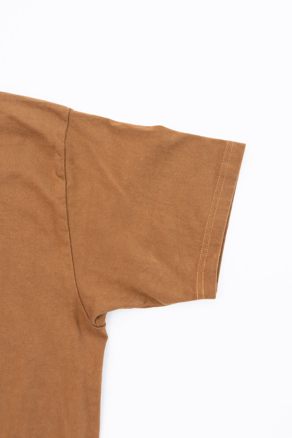 Close-up of brown short sleeve t-shirt, showing sleeve hem with contrast stitching and fabric texture.