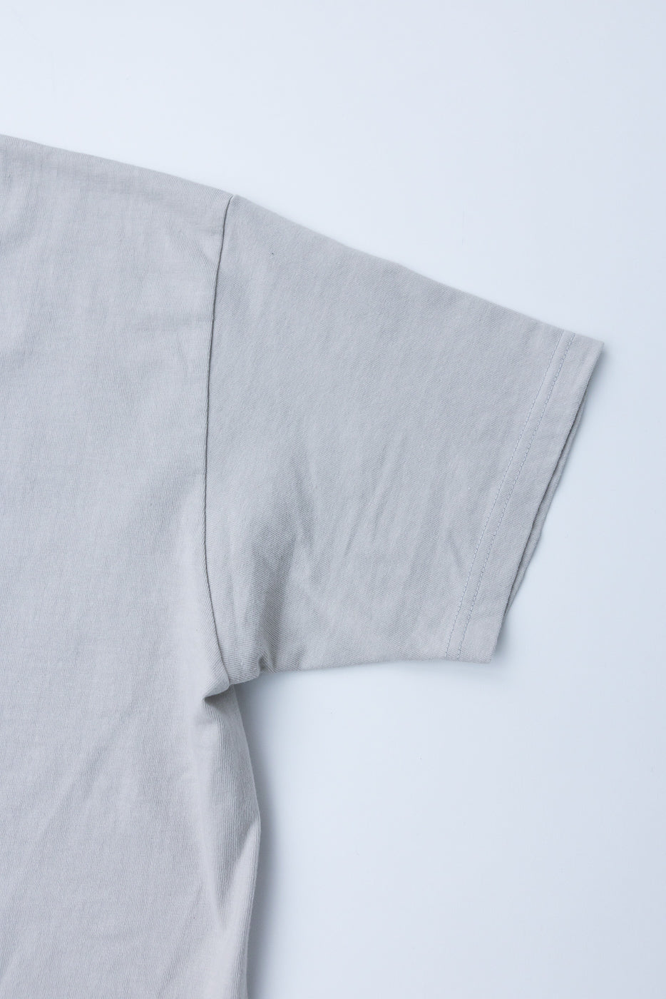 Close-up of light gray t-shirt sleeve hem, showing clean stitching and soft fabric texture, front view