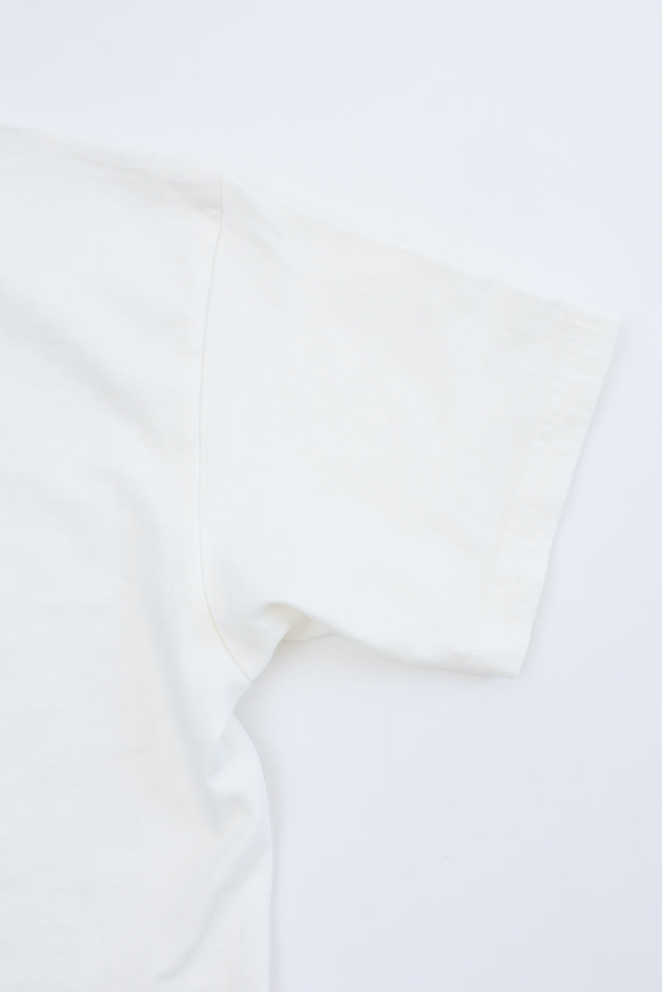 Close-up of white t-shirt sleeve and shoulder seam, front view, showing fabric texture and stitching detail