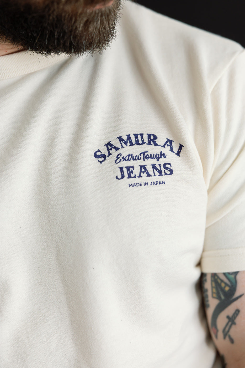 Close-up front view of male model wearing cream tee with 'SAMURAI JEANS' chest print, athletic build, 5'9