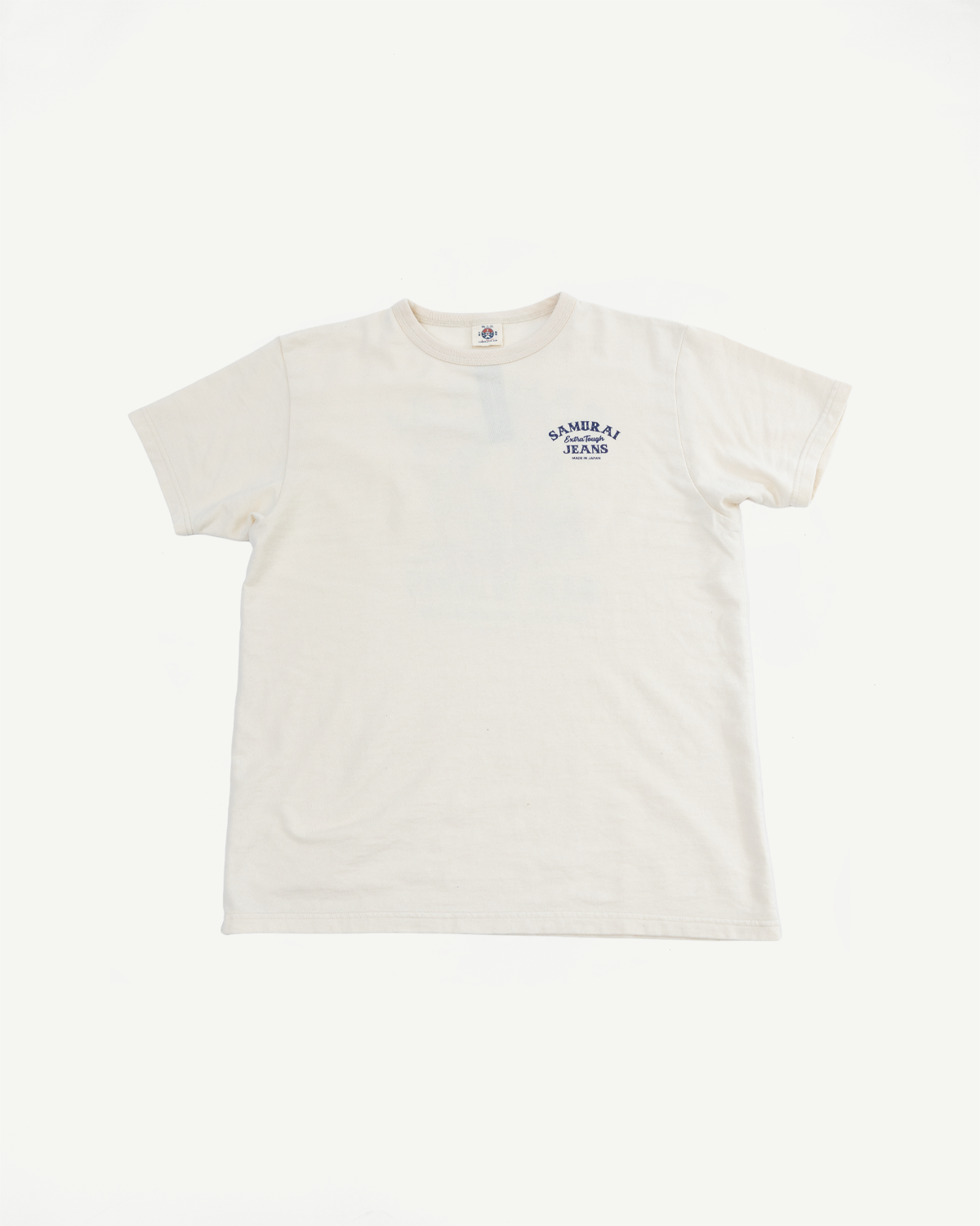 Cream short-sleeve tee, front view, featuring 'SAMURAI JEANS' chest logo and brand tag at collar, flat lay