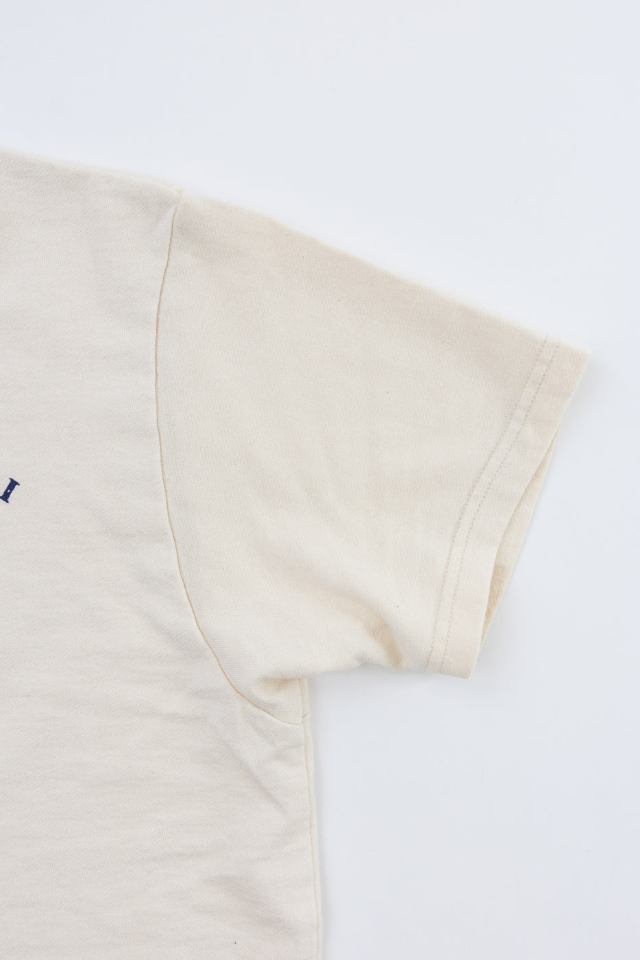 Close-up front view of cream t-shirt sleeve, showing ribbed hem and side seam detail