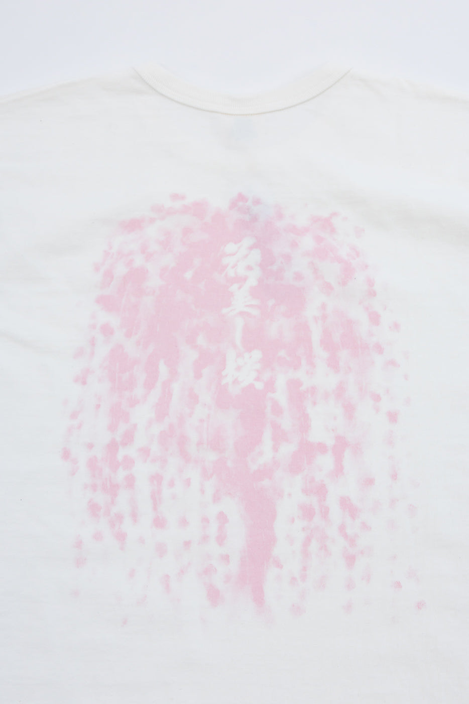 Close-up back view of white tee with pink cherry blossom print and Japanese text, soft cotton texture