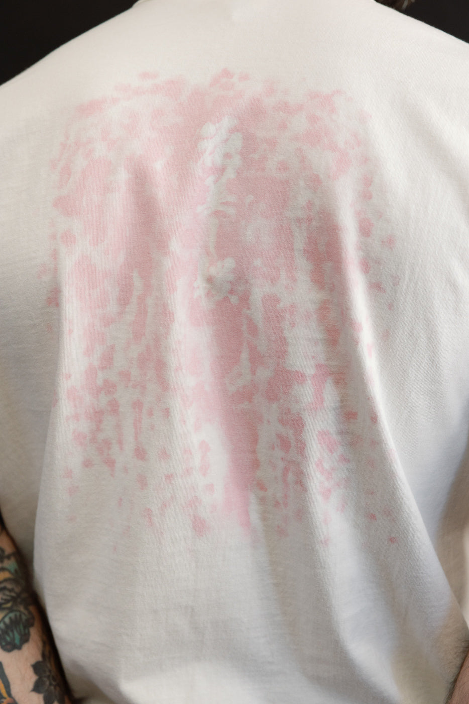 Back view of white tee with pink floral print, worn by male model, close-up on fabric texture