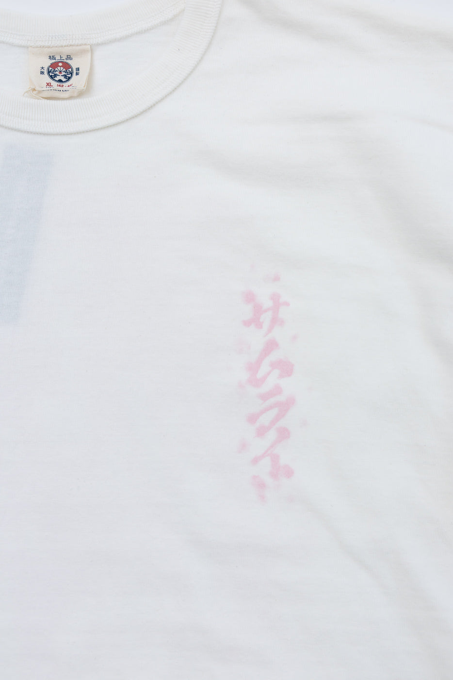 Close-up front of white tee showing pink vertical graphic print and branded neck tag, size XL