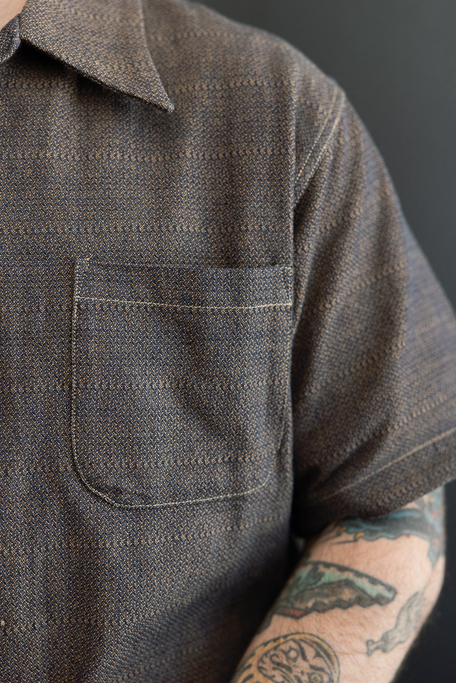 Close-up front view of men's short-sleeve shirt with chest pocket, textured fabric, and contrast stitching